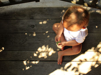 High angle view of baby holding leaf on floorboard at porch