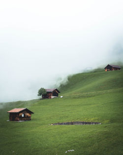 House on field by houses against sky