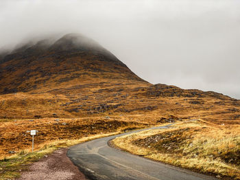 Road leading towards mountain against a misty sky