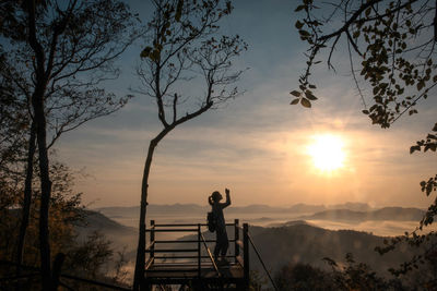 Silhouette man standing by tree against sky during sunset