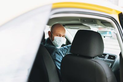 Portrait of man wearing mask sitting in car seen through window