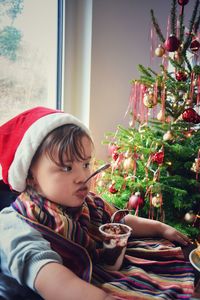 Girl eating dessert while looking away by christmas tree