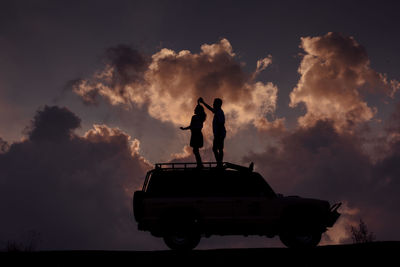 Silhouette man standing by statue against sky during sunset