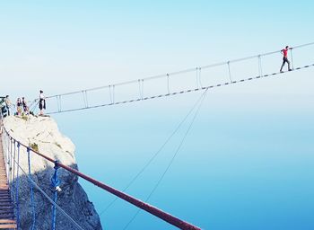 Low angle view of people walking on footbridge against sky