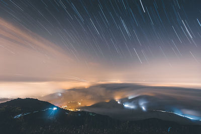 Scenic view of illuminated mountains against star trails at night