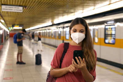 Woman using smartphone while standing at railroad station