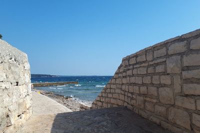 Stone wall by sea against clear blue sky