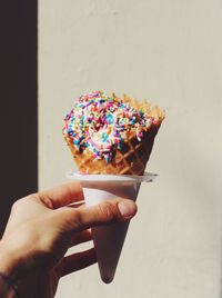 Cropped hand having ice cream cone against wall