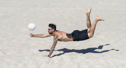 Full length of shirtless man playing with ball on beach