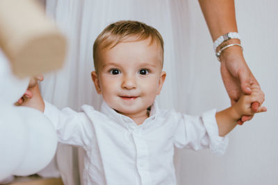 Portrait of baby boy holding hands with mother standing at home