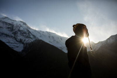 Side view of thoughtful male traveler in warm clothes standing on background of himalayas mountain range on sunny day in nepal
