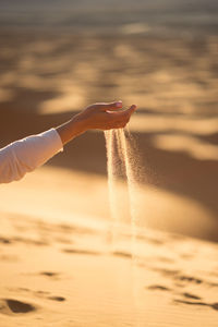 Cropped hand of person playing with sand at beach during sunset