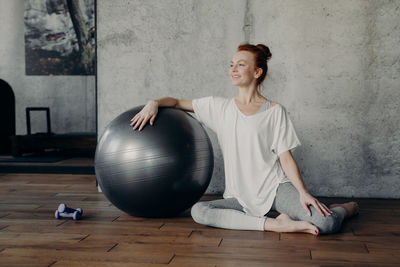 Smiling woman sitting by fitness ball at gym