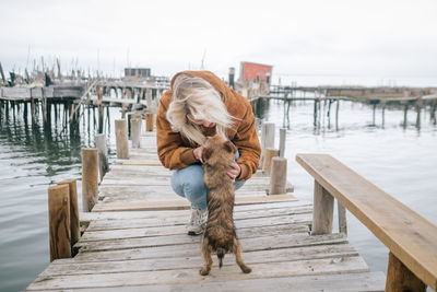 Young woman playing with dog on pier over sea