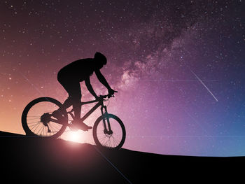 Silhouette man riding bicycle against sky at night