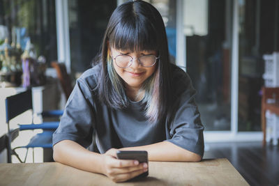 Smiling girl using mobile phone while sitting at cafe