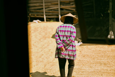 Rear view of woman wearing asian style conical hat while walking on field