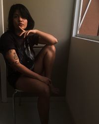Portrait of young woman with tattoo sitting on chair at home
