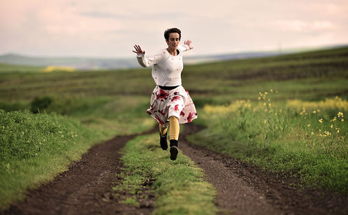 Full length of woman jumping on field against sky