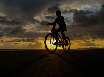 Silhouette man riding bicycle on road during sunset