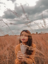 Young woman looking away while sitting on land against sky