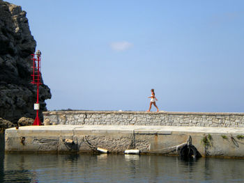 Full length of woman walking on retaining wall by lake against sky