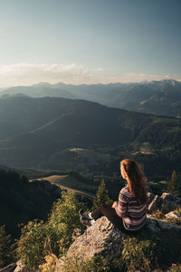 Woman sitting on mountain against sky