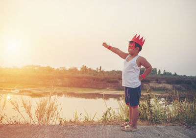 Boy wearing mask while gesturing on pier in lake against sky