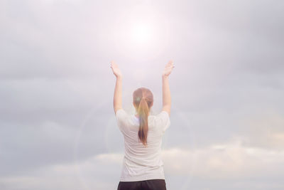 Rear view of woman with arms raised standing against sky