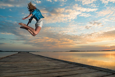 Woman jumping on beach against sky during sunset