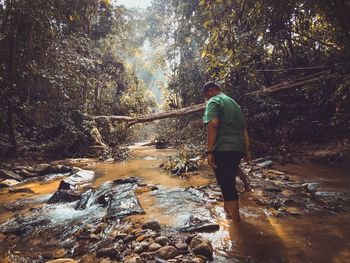 Side view of man standing in river at forest