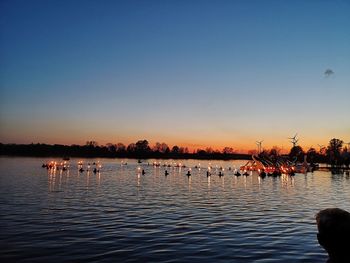 People in lake against clear sky during sunset