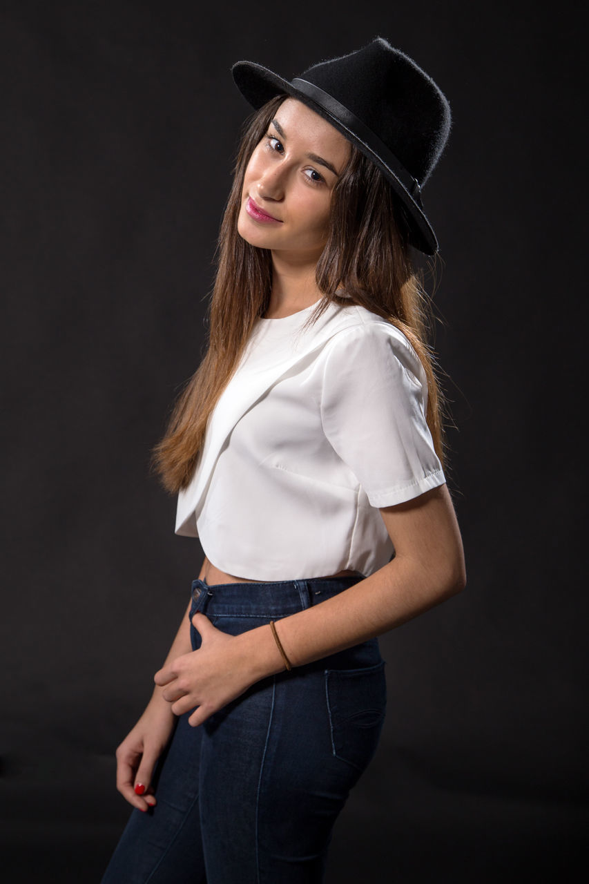 one person, hat, standing, studio shot, clothing, looking at camera, three quarter length, portrait, indoors, women, long hair, hairstyle, black background, hair, girls, casual clothing, lifestyles, leisure activity, beautiful woman, teenager