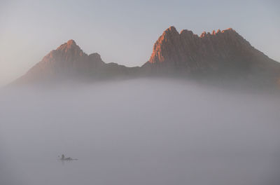 Scenic view of lake by mountains against sky during foggy weather