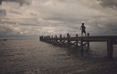 Rear view of boy running on pier over sea against cloudy sky during sunset