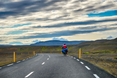 Rear view of men riding bicycle on road against sky