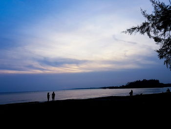 Silhouette people on beach against sky during sunset