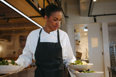 Female chef holding salad bowls in hand at commercial kitchen