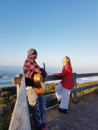 Man playing guitar while woman listening against clear sky