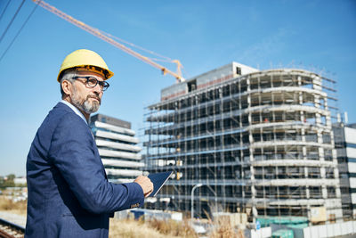 Businessman wearing hardhat while standing against built structure