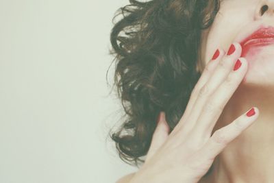 Cropped image of woman spreading red lipstick against white background