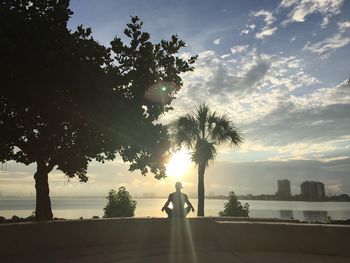 Silhouette man doing yoga by lake against sky