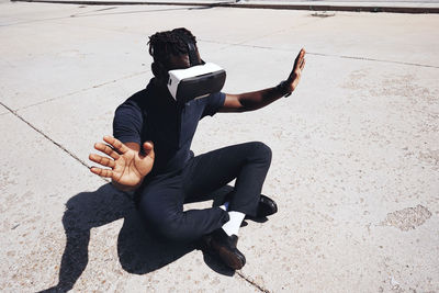 High angle view of teenager gesturing while using virtual reality on road during sunny day