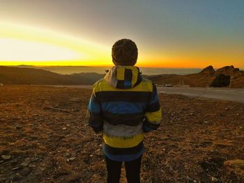 Rear view of man standing on land against sky during sunset