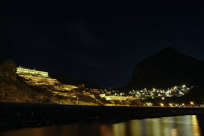 Illuminated city by river against sky at night