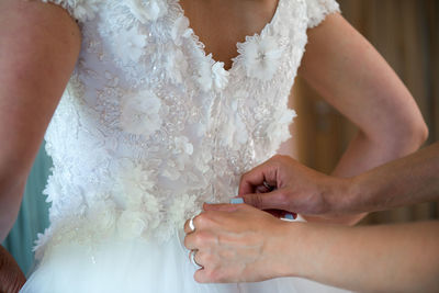 Cropped hands of woman helping bride in getting dressed