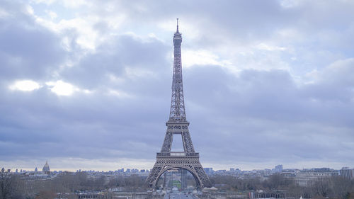 Communications tower in city against cloudy sky