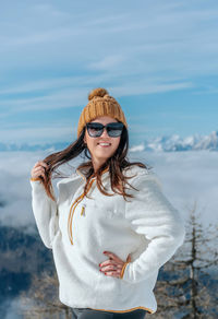 Portrait of beautiful happy girl wearing winter clothes, standing in amazing mountains on sunny day