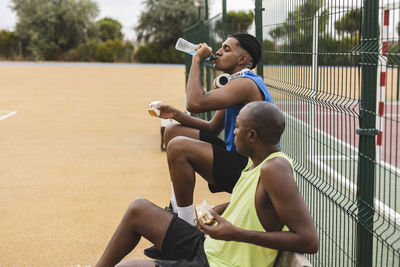 Young man drinking sports drink sitting by father on bench