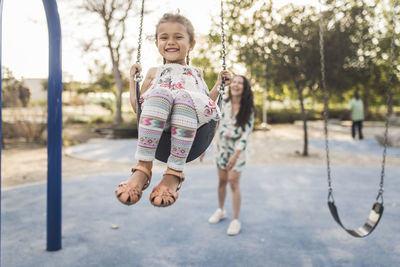 Happy mother pushing cute daughter swinging at playground